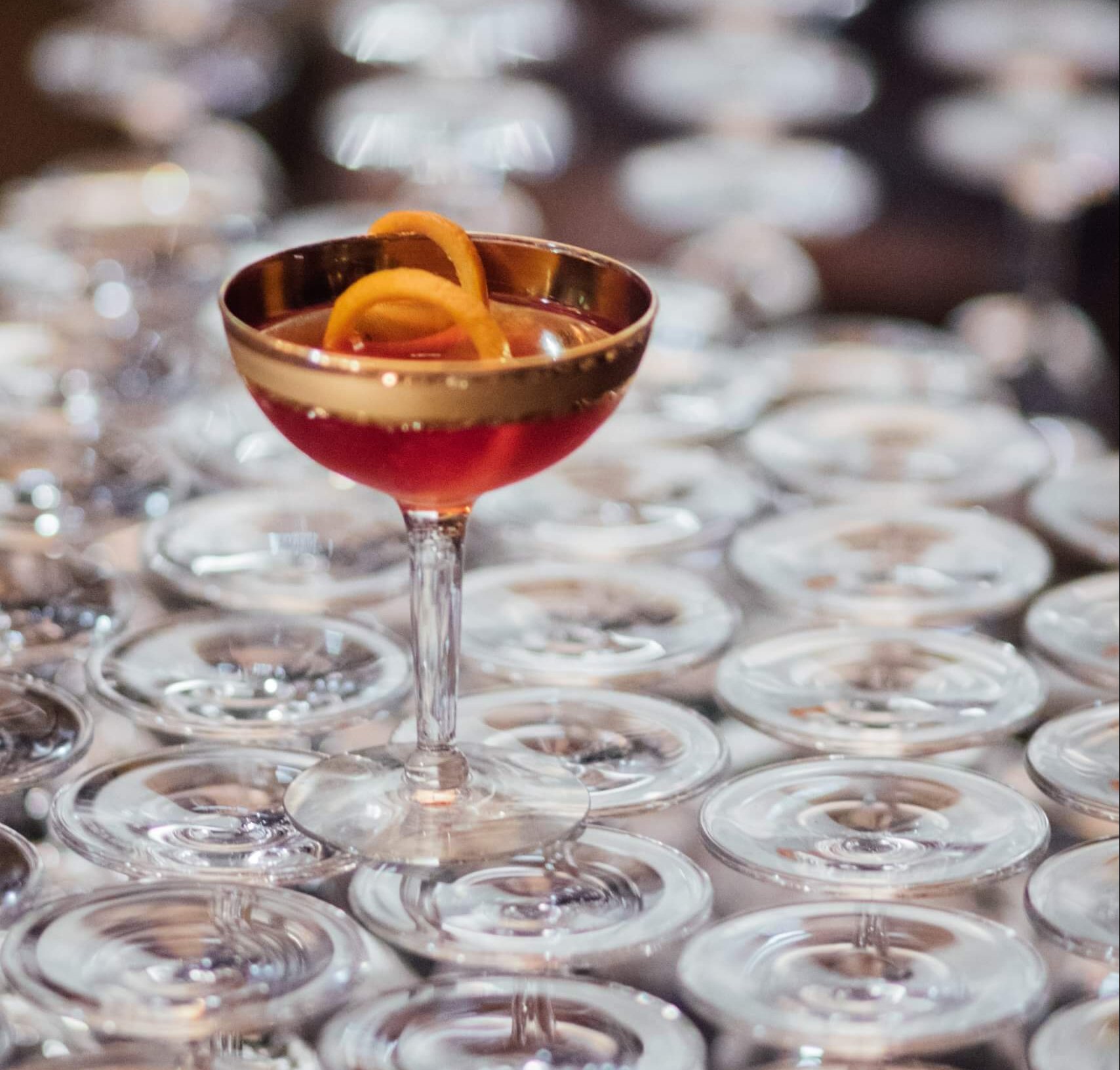 A coupe glass with orange rind and red cocktail on top of stacked glasses.