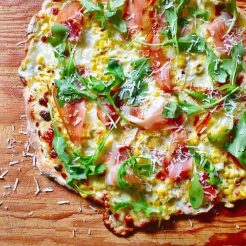 A pizza topped with arugula and tomatoes on a wooden board.