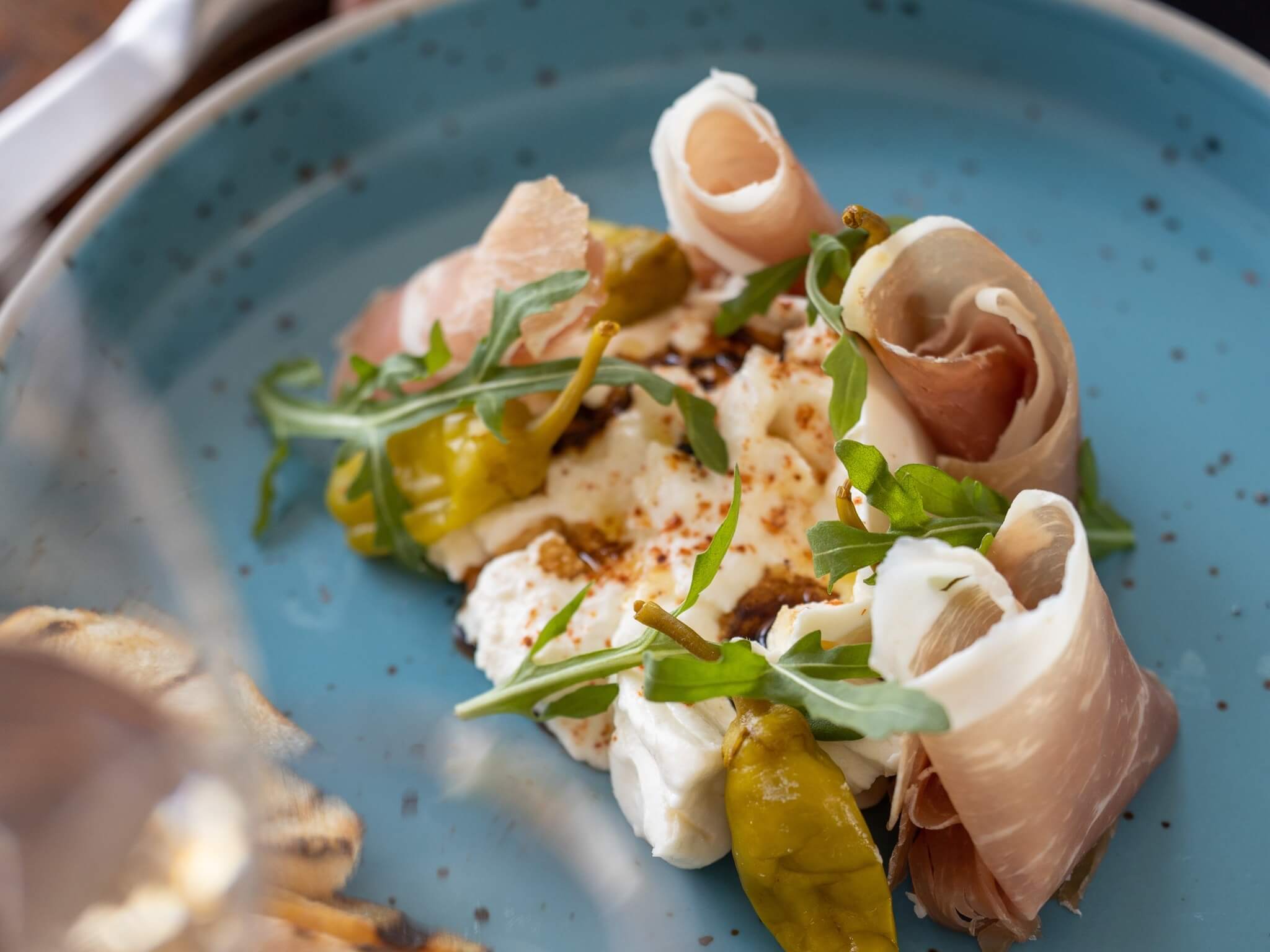 A blue plate with a fresh cheese and prosciutto dish