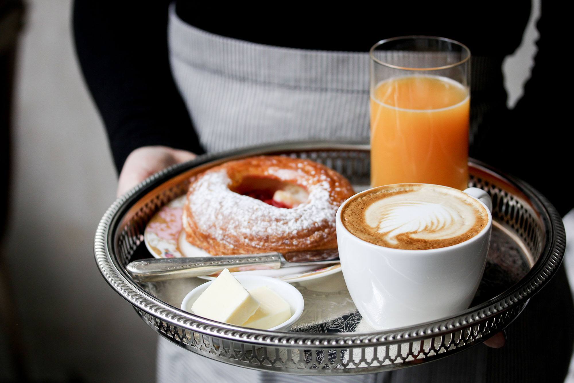 A woman holding a tray with a pastry, coffee and glass of juice