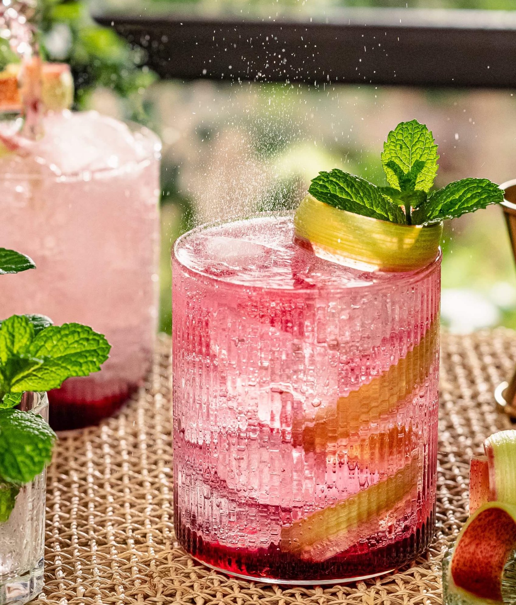 rhubarb cocktail with tonic on rug backgroun styled in garden, sunlight
