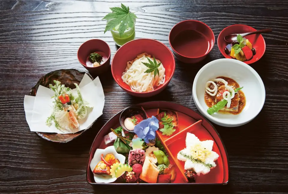 A dark wood table laid with red dishes containing Japanese food