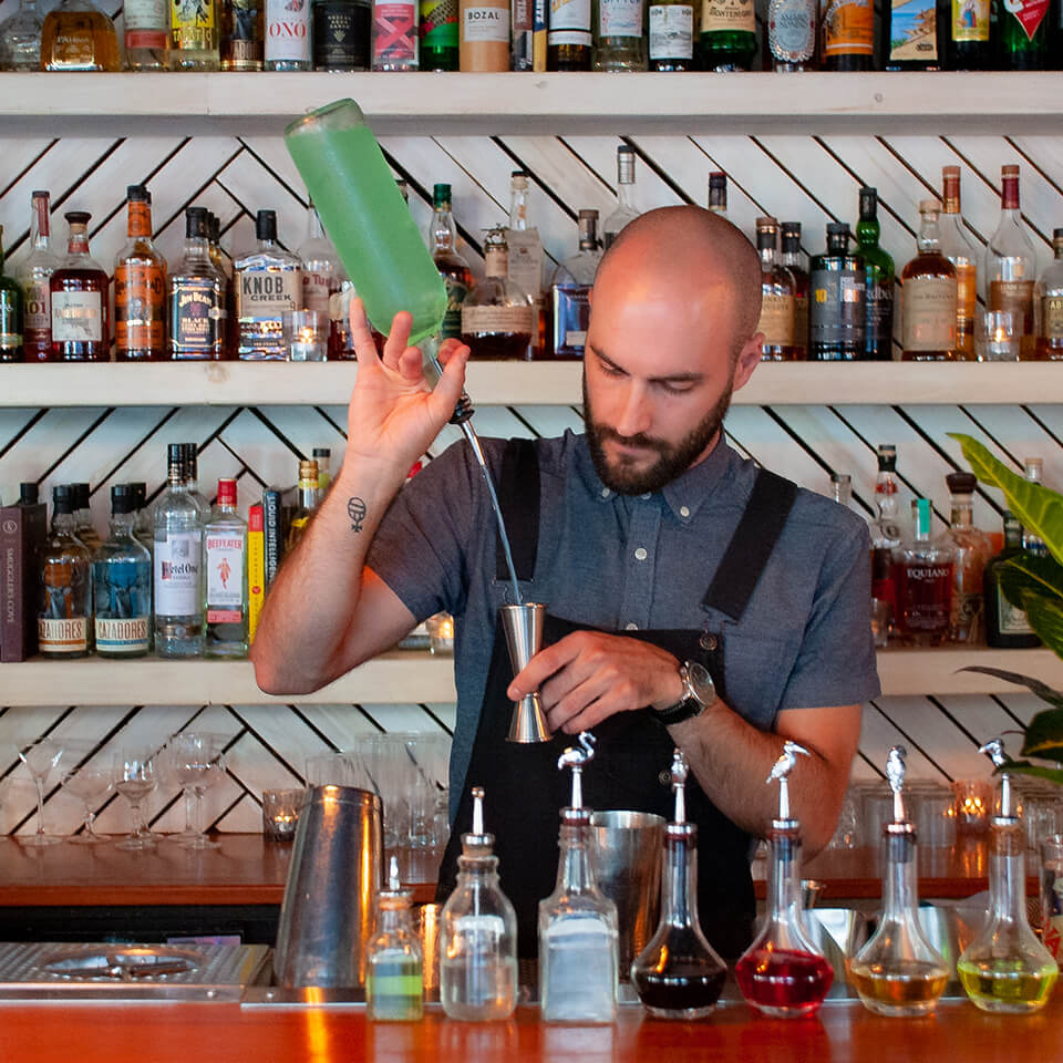 A man, Stéphane Duval, pours from a bottle into a bar measure behind a bar counter