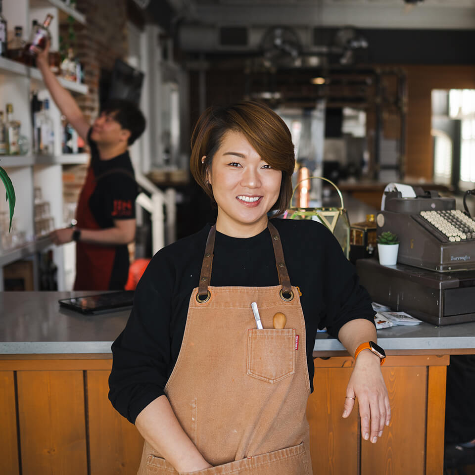 A woman, Jinhee Lee, smiling in front of a bar in a restaurant