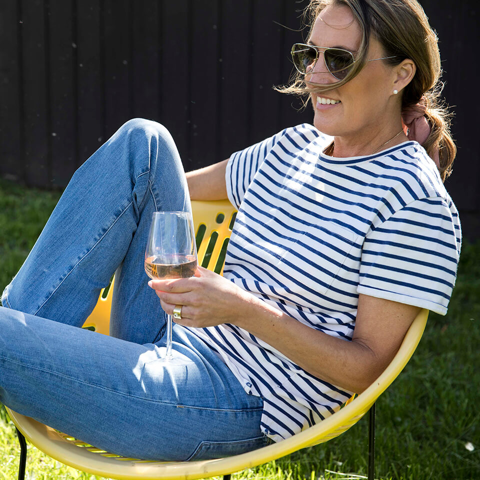 A woman, Sarah Bancroft, sitting in a yellow patio chair with a glass of wine