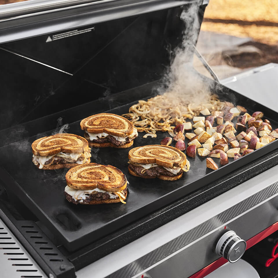 Sandwiches, potatoes and onions cooking on an outdoor griddle
