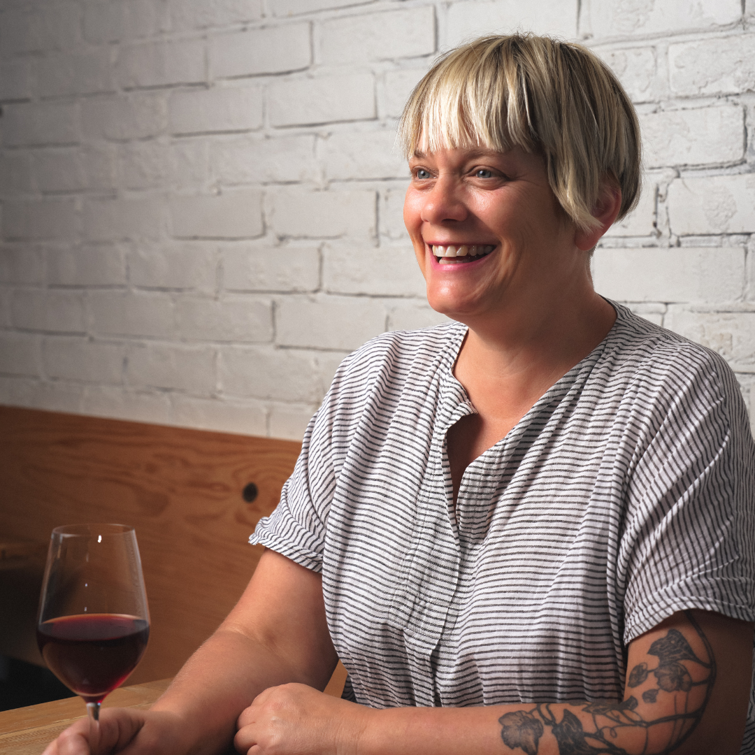 Blonde woman with a bob holding a wine glass and smiling.