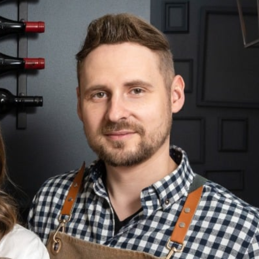 Bearded man wearing a checkered shirt and brown apron.