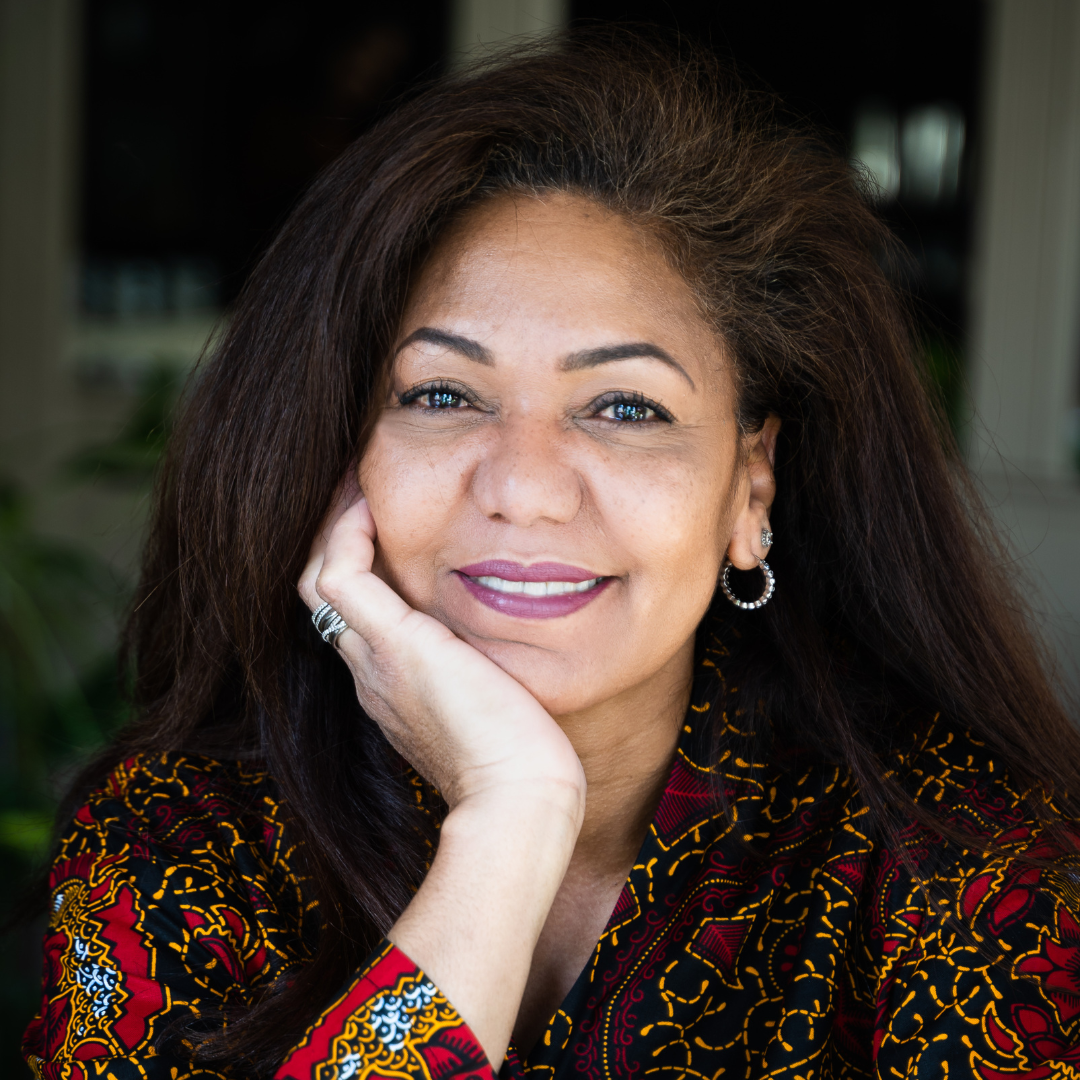 A woman with brown hair smiling and resting her chin on her palm.