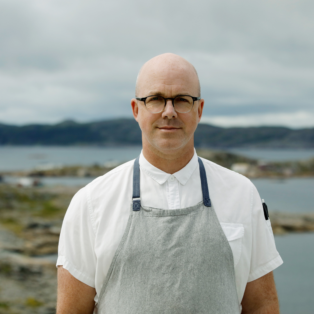 A bald man wearing glasses and a white shirt and apron.