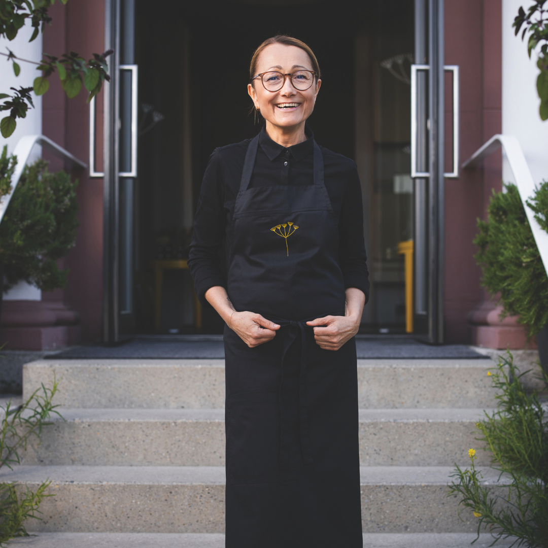 A smiling woman in a black shirt and apron.