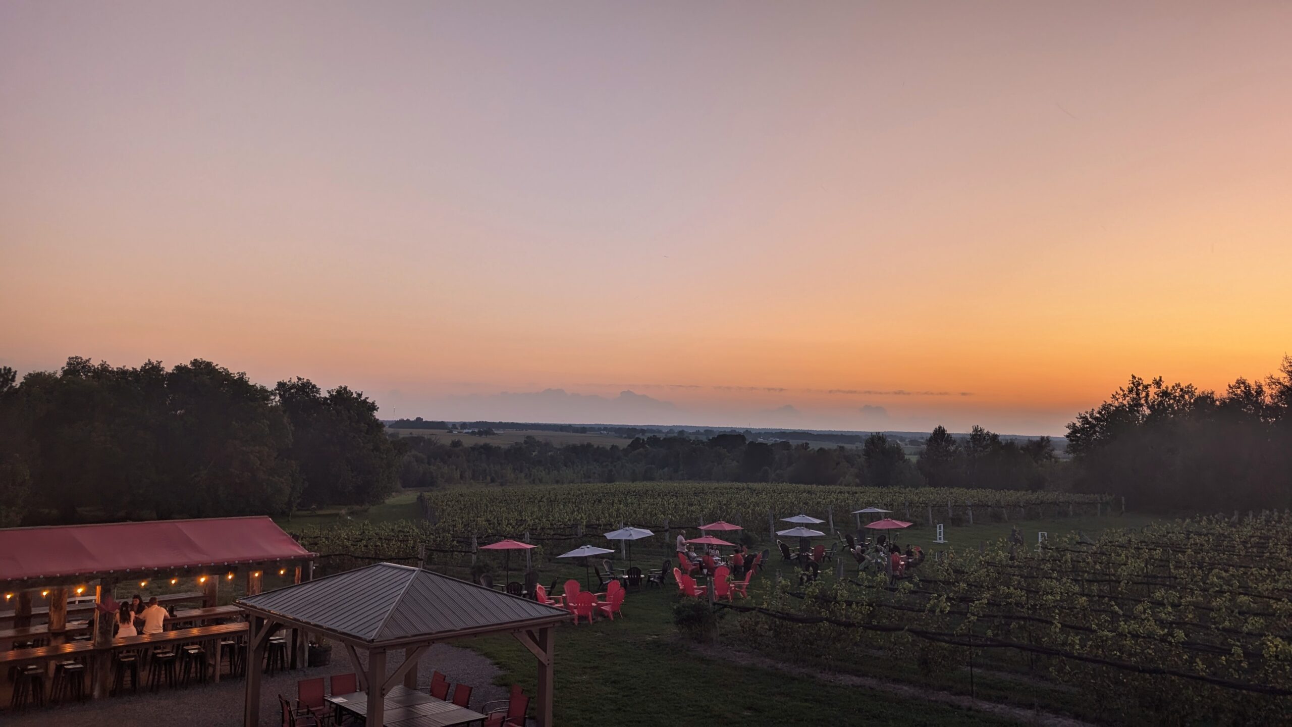 Orange sunset over a vineyard with red outdoor seating.