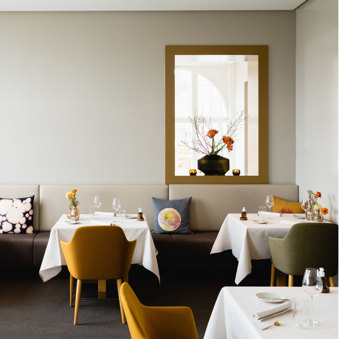 Restaurant interior with yellow chairs and tables with white tablecloth.