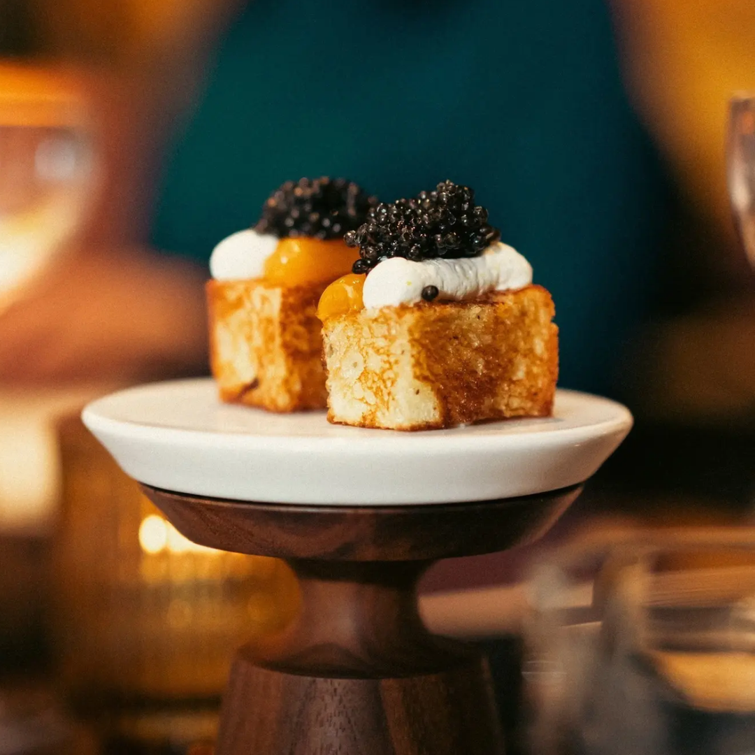 Two pieces of potato topped with caviar and creme fraiche on a stand.