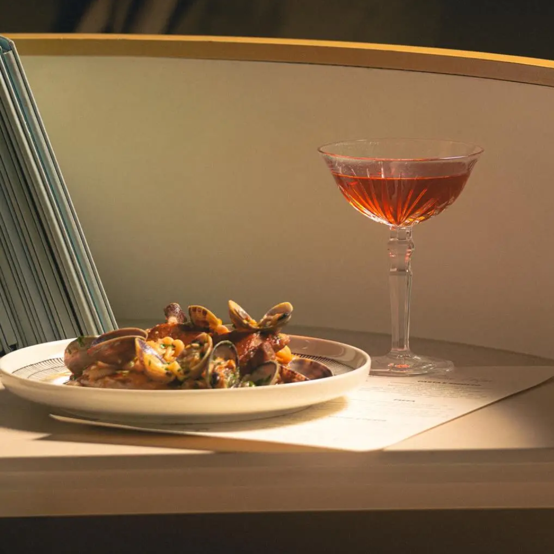 A cocktail next to a small plate on a table.