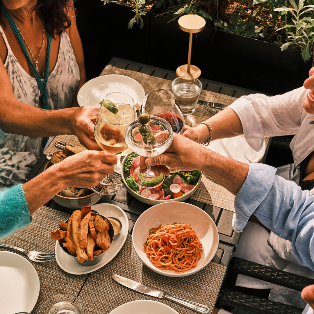 Hands holding wine glasses clinking over a dinner table with small plates.