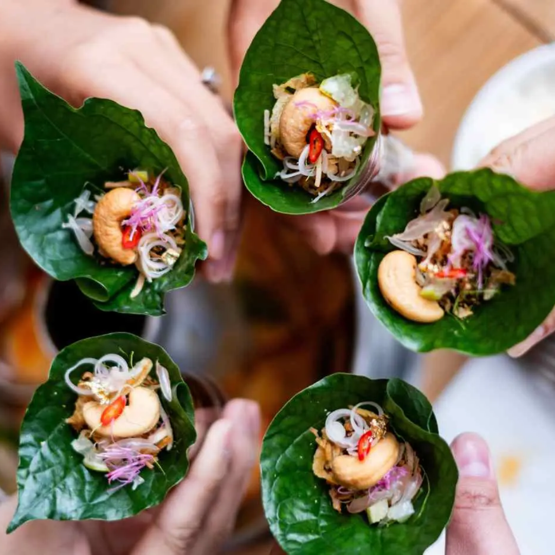 Hands holding a Thai salad wrapped into a bamboo leaf cone.