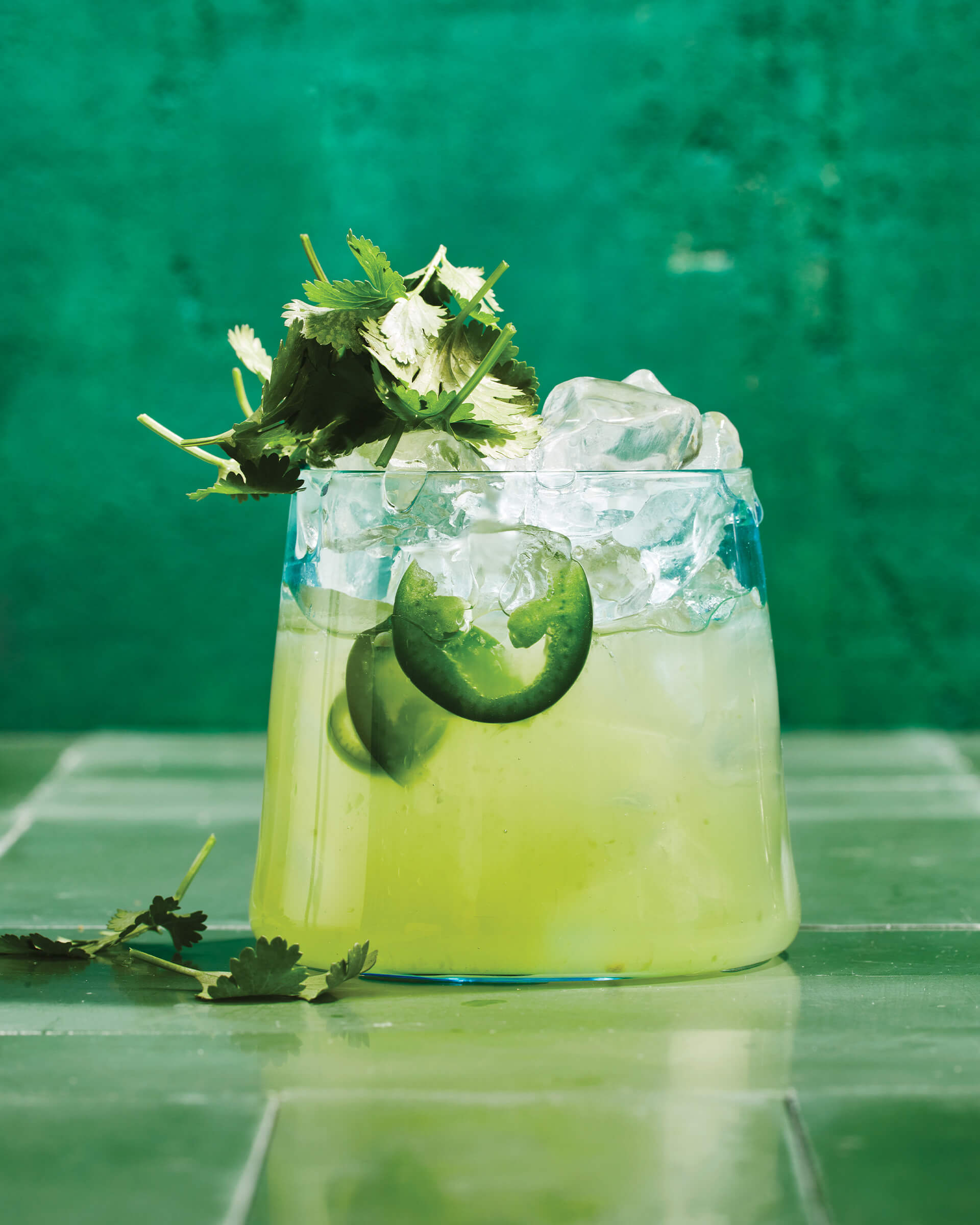 A short glass of limeade against a green backdrop.