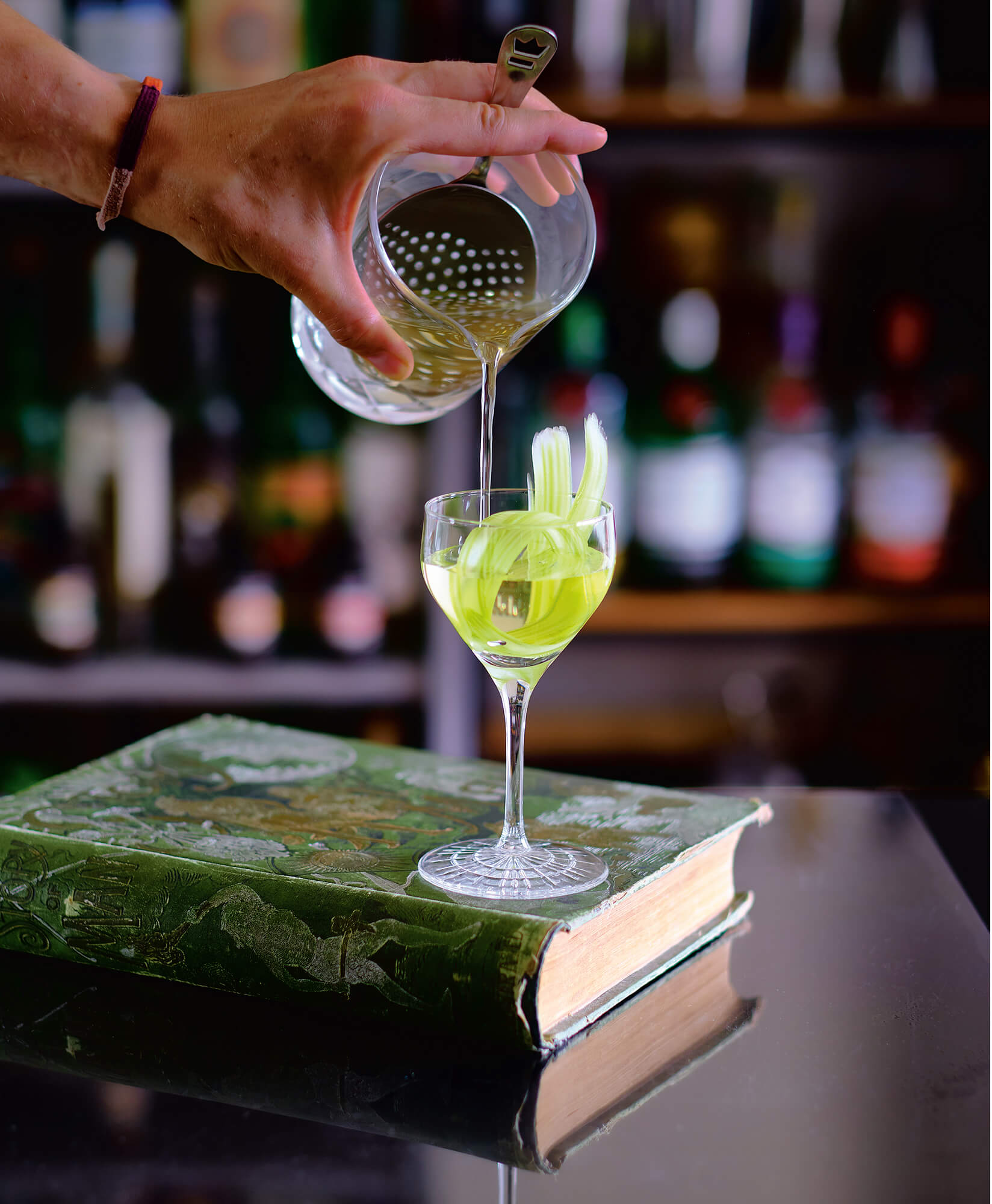 A cocktail is poured into a glass on top of a book