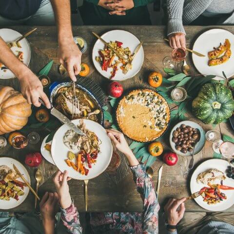 A wooden table topped with pie, pumpkins and plates of food.