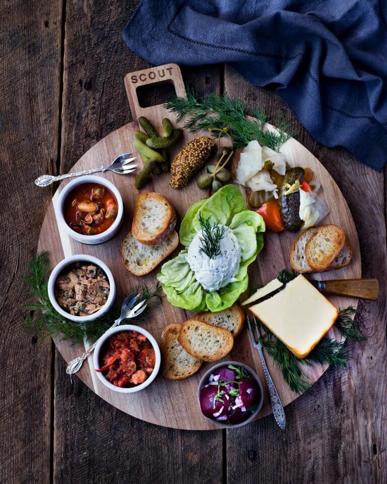 A board with three bowls of seafood, cheese and vegetables shot from above
