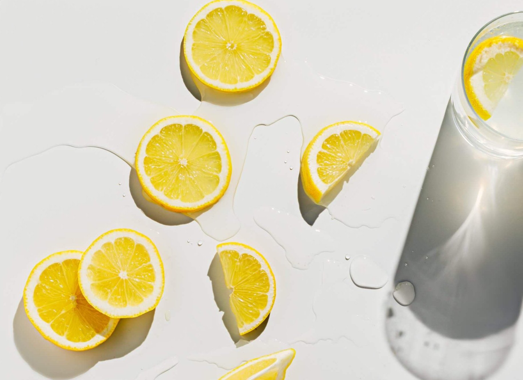 Fresh lemons cut into slices on bright white wet surface with gl