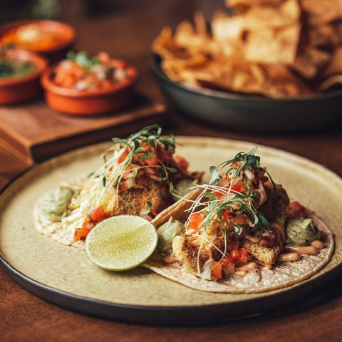 A plate with Fish tacos with chipotle mayo, pico de gallo and avocado mousse on a wooden table