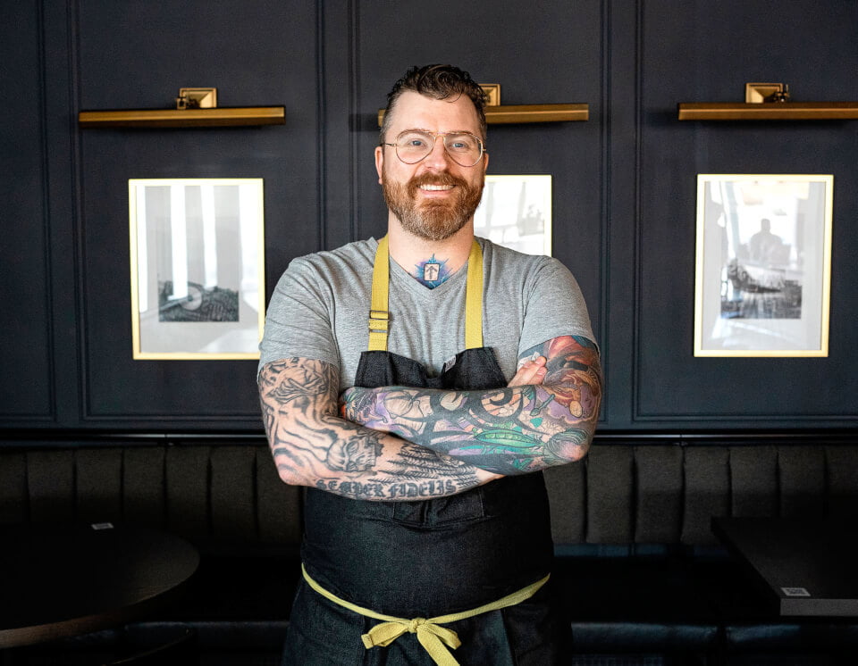 A man, Gus Stieffenhoffer-Brandson, crosses his arms and smiles at the camera