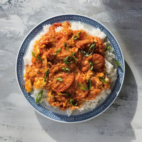 A blue dish with rice and a tomato-egg stir-fry on a grey surface