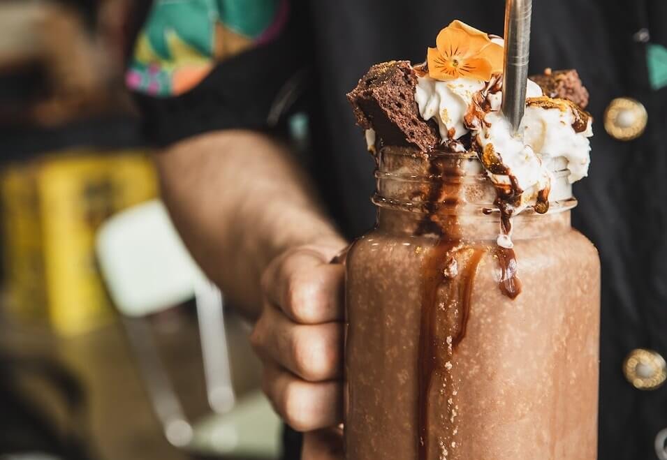 A person holding a chocolate milkshake with elaborate toppings