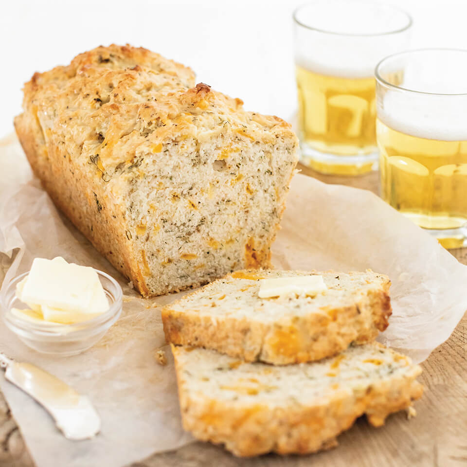 A loaf of sliced beer cheeese bread with glasses of beer in the background