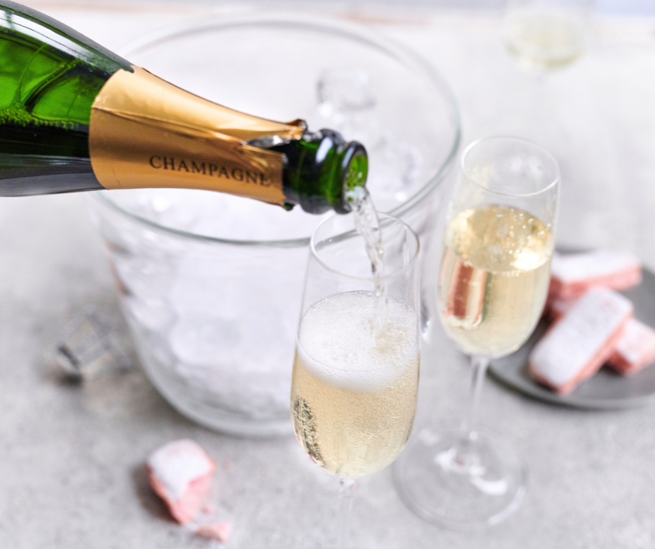 A bottle of champagne is open and the champagne is pouring into crystal stemmed glasses. 