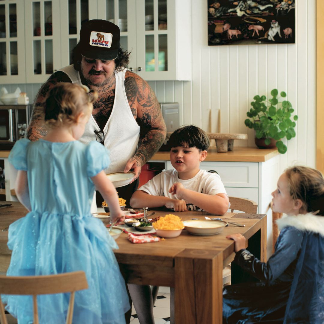 Matty Matheson (tattooed man) serves mac and cheese to his three children at the dinner table.