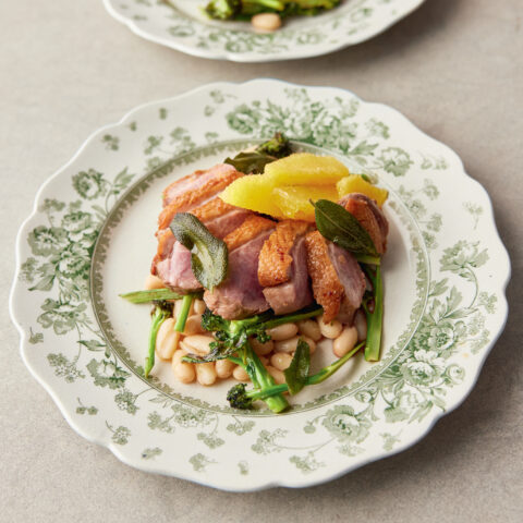 White plate topped with crispy duck, creamy white beans and charred broccolini.