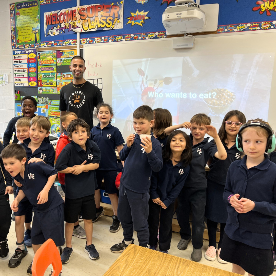 Chef Imrun Texeira stands with 13 children in front of a white board in a classroom.