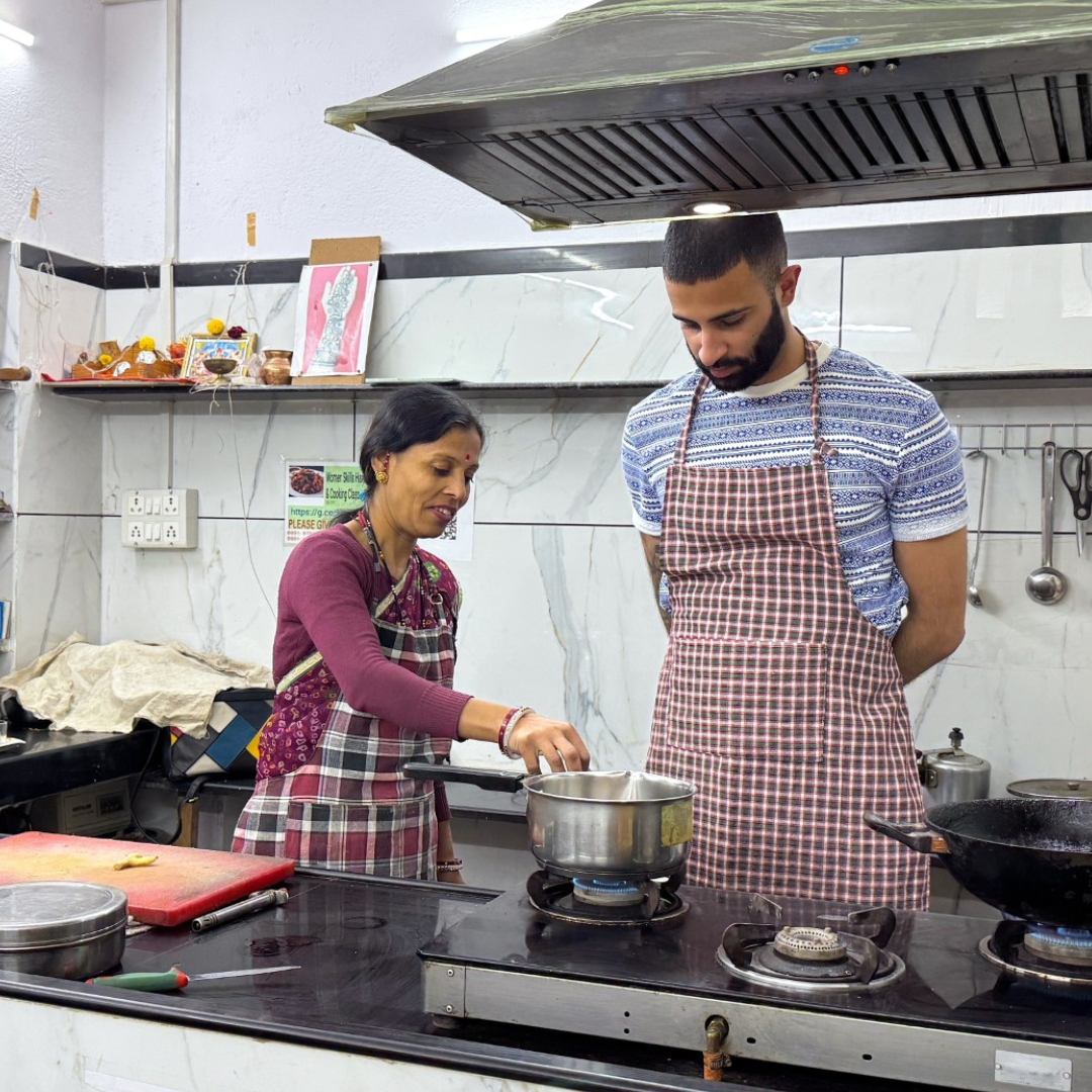 An aproned woman teaches chef Imrun Texeira in the kitchen. 