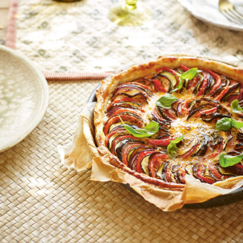 Vegetable-topped ratatouille quiche with a golden crust in a baking dish at a table setting.