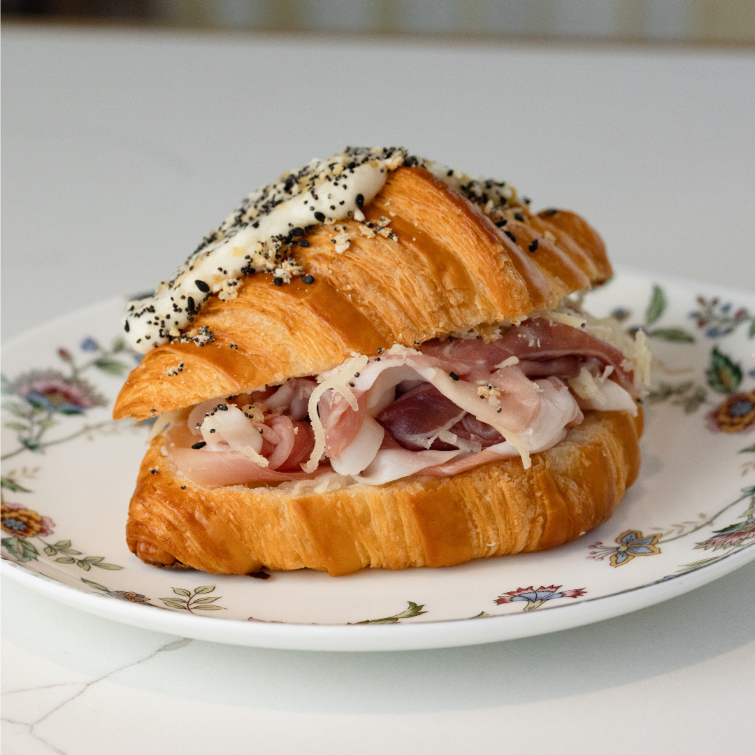 A croissant topped with everything bagel spice and filled with ham and cheese inside. 